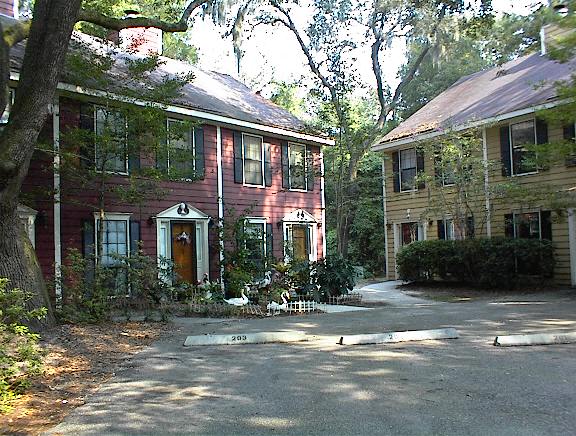 A red house with a white door and windows is surrounded by trees.